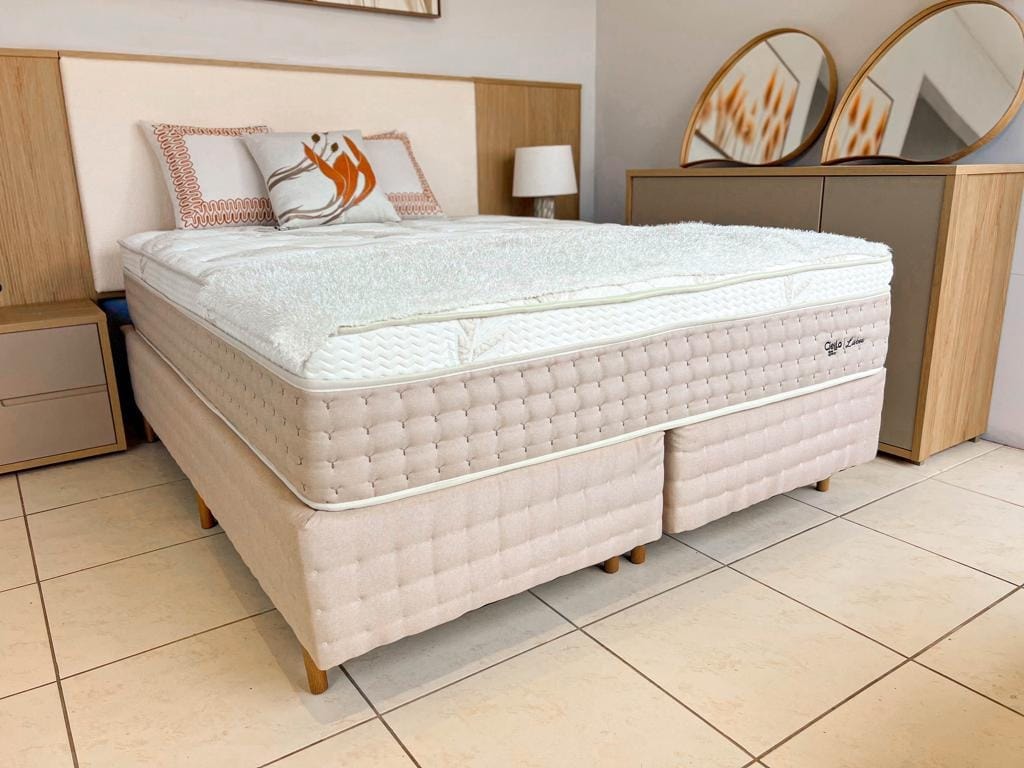 Cama box de casal Lisboa com base cinza e colchão alto, ambientada em um quarto elegante com decoração em tons neutros e painel ripado.