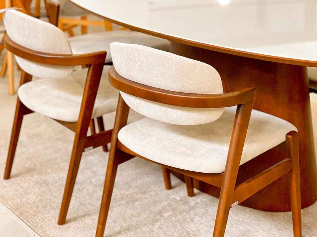 Conjunto de mesa de jantar clara com base de madeira e cadeiras estofadas em tom neutro, ambientado em uma sala de jantar moderna.