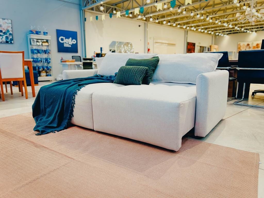 Sofá cama cross bege com almofadas verdes em ambiente.