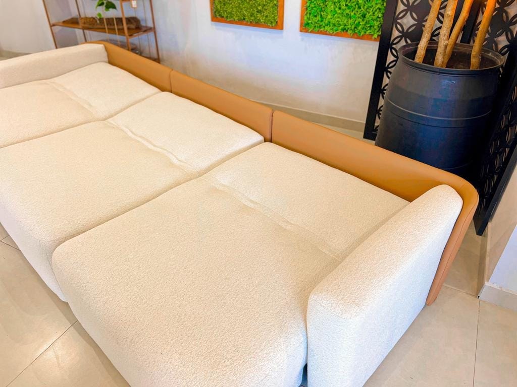 Visão frontal do sofá retrátil Empíreo na cor neutra, destacando o design curvo dos braços e o acabamento premium em uma sala elegante.