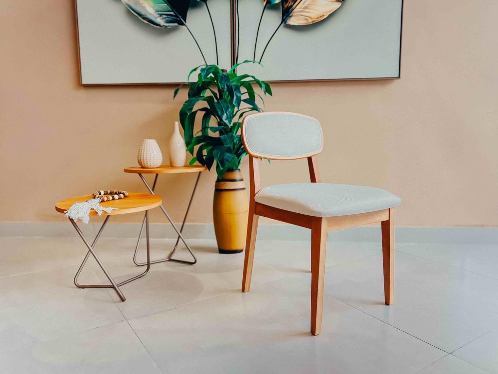 Cadeira Dina estofada na cor clara, mostrando a frente do assento e a estrutura dos pés em madeira cor mel.