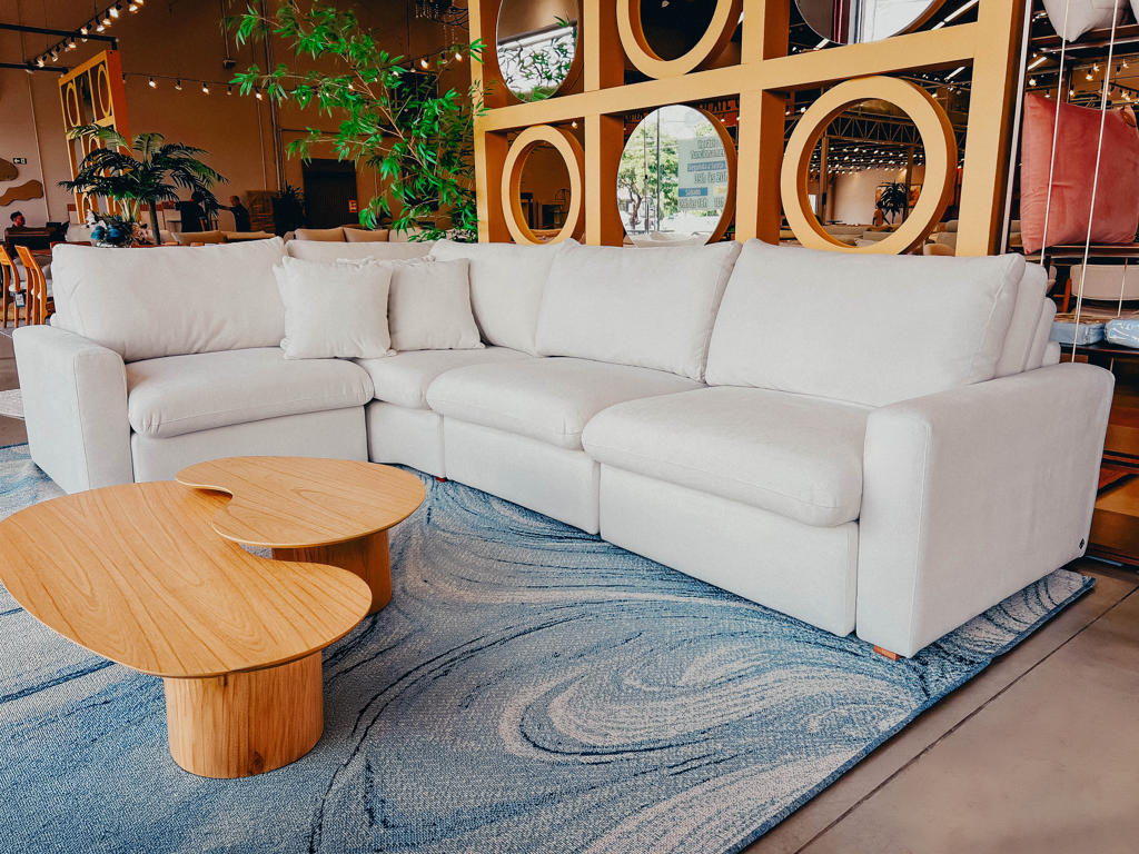 Visão frontal do Sofá Slow em tecido bouclé ou texturizado off-white. Possui formas arredondadas, braços baixos e volumosos e assento profundo, em um ambiente decorado com tapete neutro.