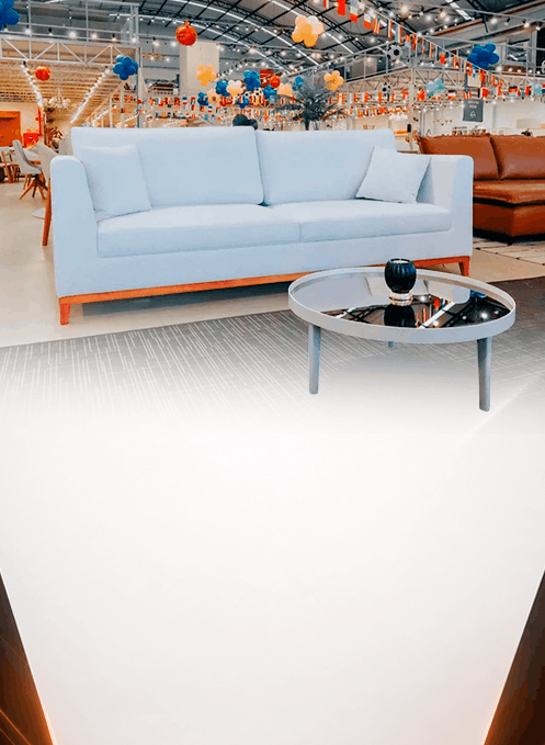 Light blue sofa on a showroom floor with a round glass coffee table in front and colorful decorations overhead.