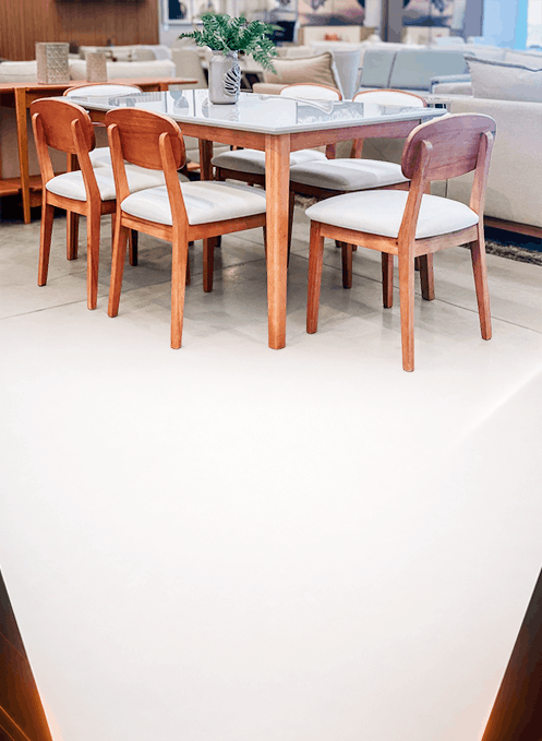 Wooden dining chairs surrounding a glass-top table with a small potted plant centerpiece in a bright showroom.