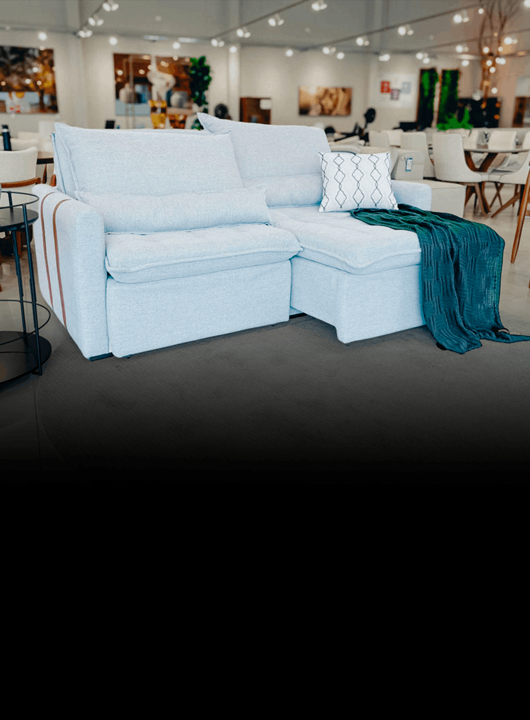 Light blue fabric sectional with chaise in a showroom, teal blanket draped over end and a patterned pillow on the seat.