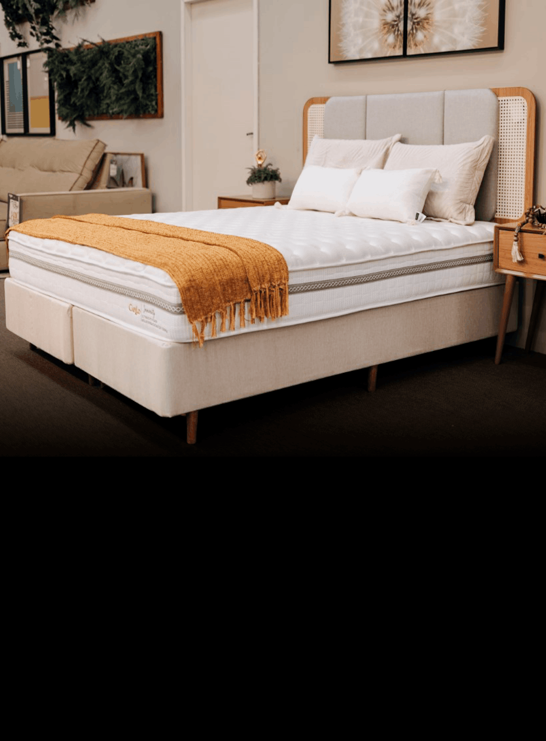 Modern bedroom showroom: a plush beige bed with white bedding, orange throw, and matching nightstands on each side.