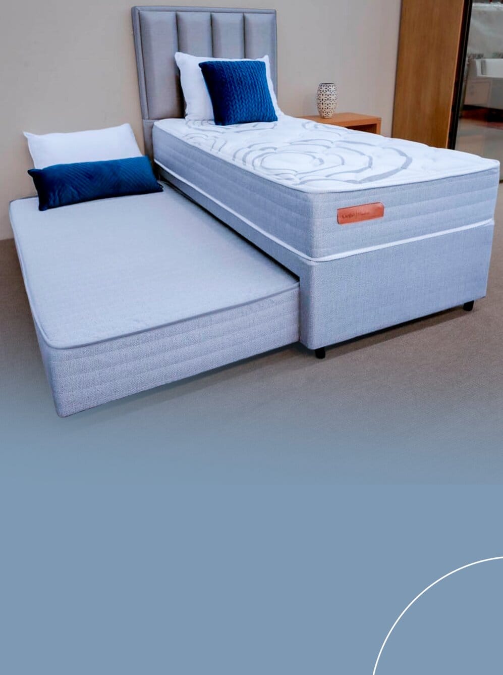 Cama box de solteiro em tecido cinza com a cama auxiliar puxada na parte inferior e cabeceira alta estofada com gomos verticais.