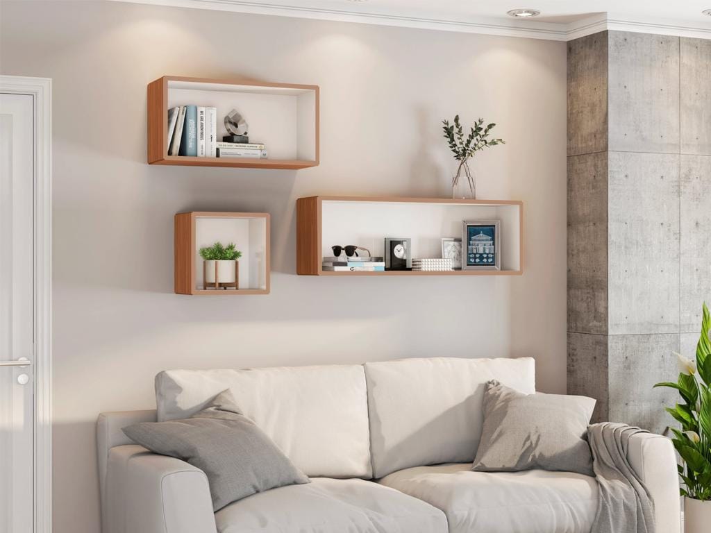Conjunto de Nichos de Parede MDF TB150 Series | Ciello Decoração de sala de estar moderna com um sofá claro e almofadas cinzentas. Na parede bege superior, estão instalados três nichos de MDF amadeirados modulares da linha TB150 em posições diferentes, decorados com livros, quadros e plantas.