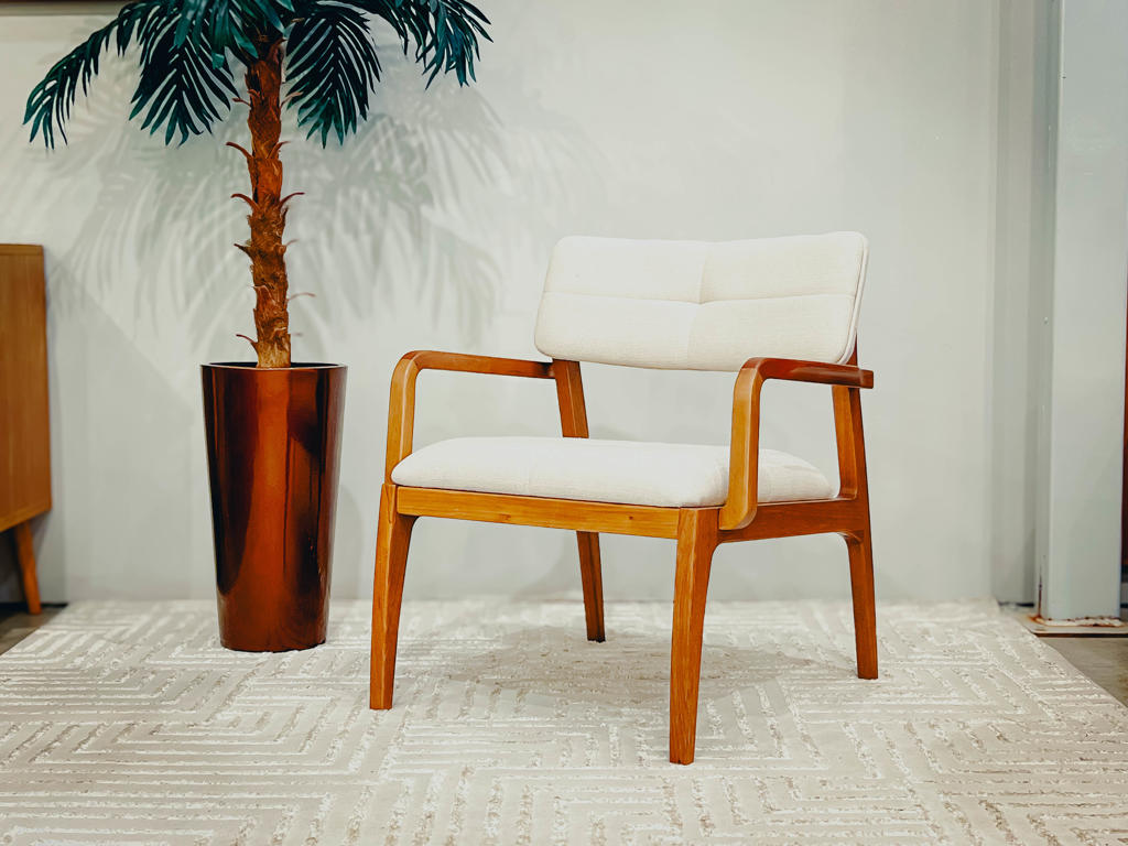 Poltrona Decorativa Design Assinado Mentha | Ciello Visão frontal angulada da Poltrona Mentha completa, evidenciando a harmonia entre o estofado claro e a estrutura de madeira, ambientada sobre um tapete neutro com uma planta ao fundo.