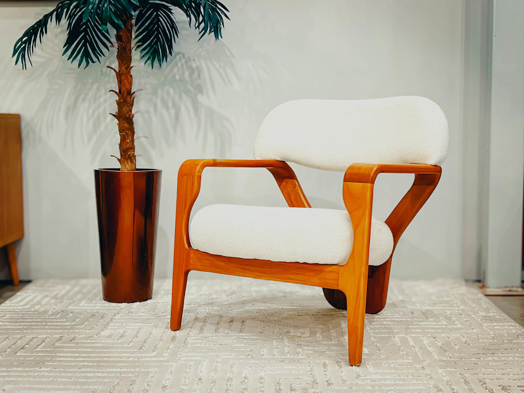 Poltrona Premiada Corpore YE Design | Ciello Visão frontal completa da Poltrona Corpore com estofamento Bouclé claro e estrutura fluida de madeira de Jequitibá, posicionada ao lado de uma planta em um ambiente decorado de alto padrão.