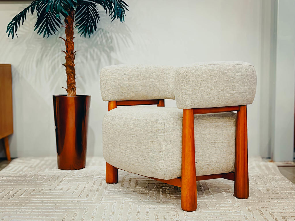 Poltrona Tauru para Sala de Estar Moderna | Ciello Móveis Poltrona Tauru bege ambientada em uma sala de estar decorada sobre tapete com relevos geométricos brancos e um vaso de bronze com planta ornamental ao fundo.