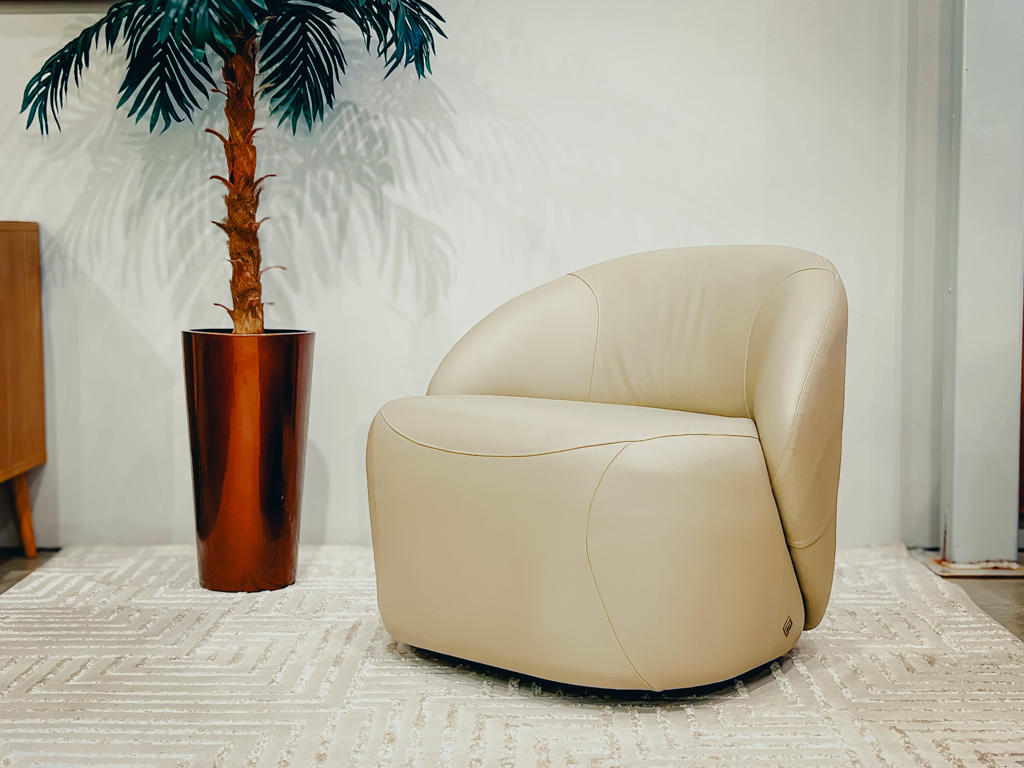 Poltrona Zoe Vista Lateral Design Orgânico | Ciello Foto em perfil lateral esquerdo da Poltrona Zoe bege, mostrando a curvatura contínua do encosto que desce até a base fixa inferior negra.