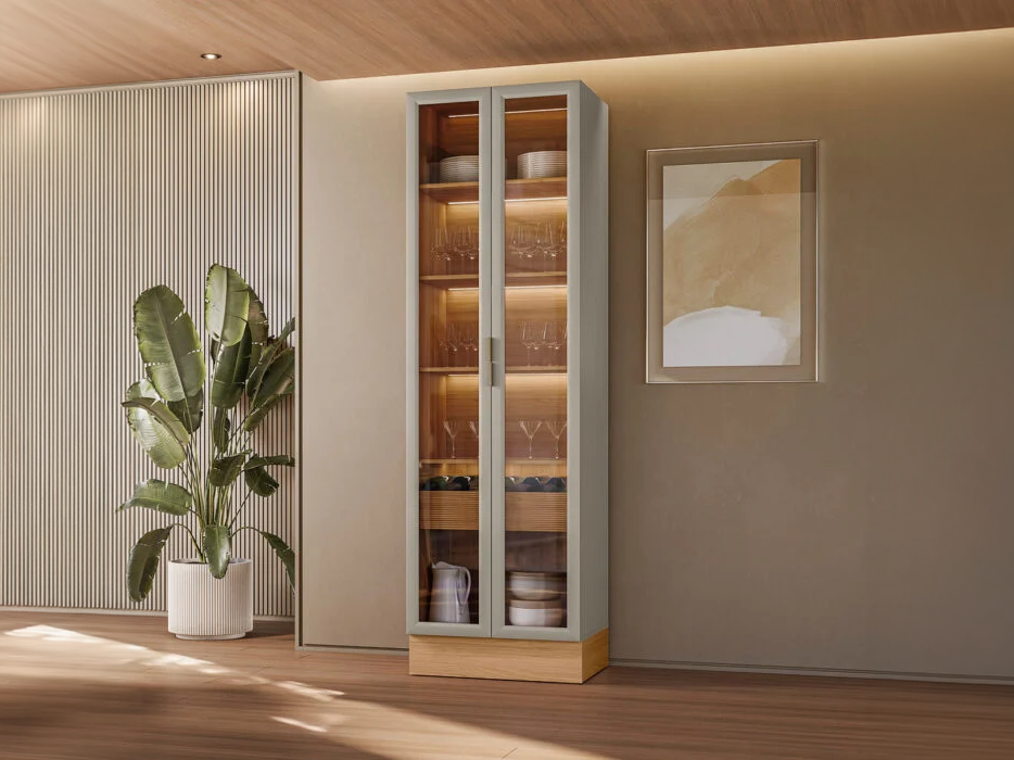Cristaleira Allure Moderna Sala de Jantar Vista frontal da Cristaleira Allure alta de duas portas de vidro ambientada em uma sala de jantar moderna de parede bege, ao lado de um vaso com planta ornamental.