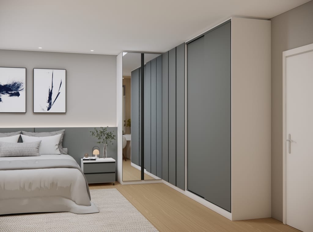 Quarto de casal contemporâneo com mobiliário modulado em formato de L. À direita, um roupeiro espaçoso apresenta caixaria branca e portas de correr em tom cinza fosco. No canto do ambiente, destaca-se um módulo com portas revestidas a espelho que reflete o quarto. À esquerda, uma cama com cabeceira cinza e uma mesa de cabeceira com gavetas no mesmo padrão de cores, sob uma parede decorada com quadros abstratos.