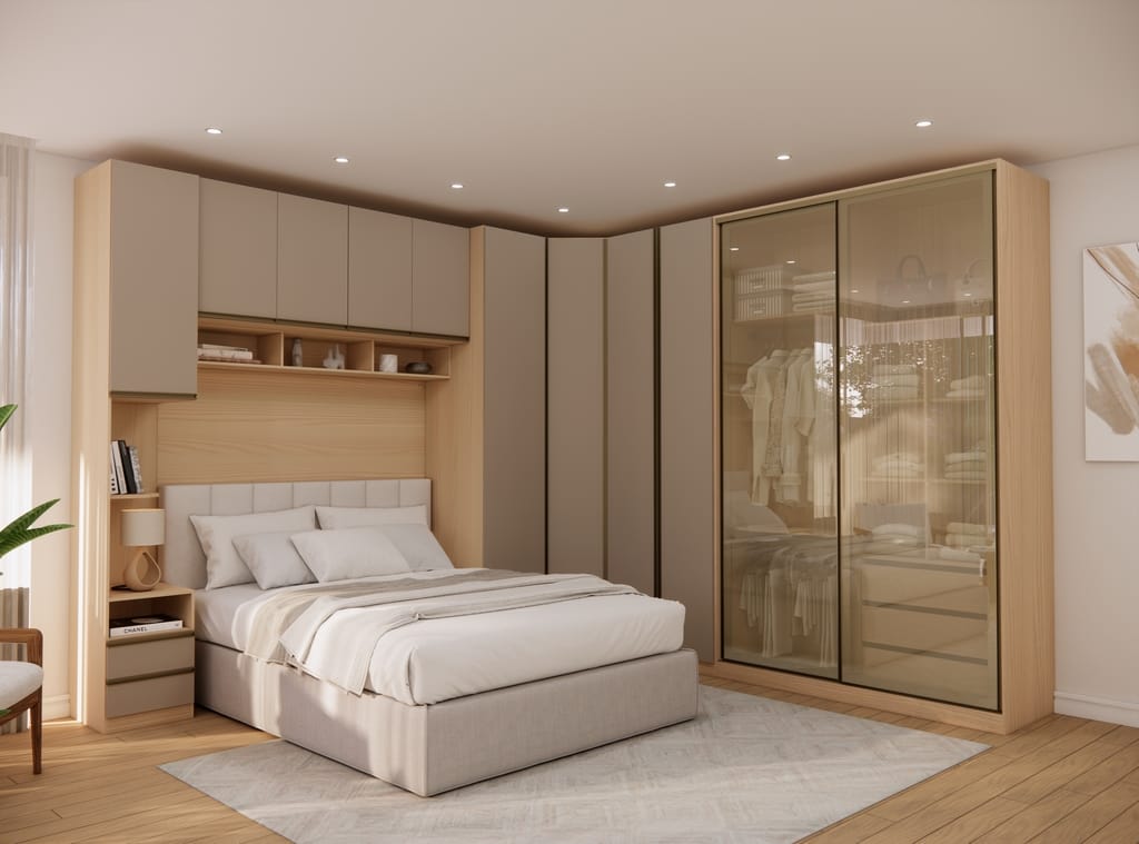 Quarto Modulado Casal Porta Vidro Reflecta uarto de casal decorado com móveis modulados em formato de L. À direita, um grande guarda-roupa possui portas de correr em vidro reflecta bronze que revelam roupas em cabideiros. Ao centro, uma cama de casal com cabeceira estofada está posicionada sob um conjunto de nichos de madeira clara e armários aéreos fechados em tom fendi fosco.