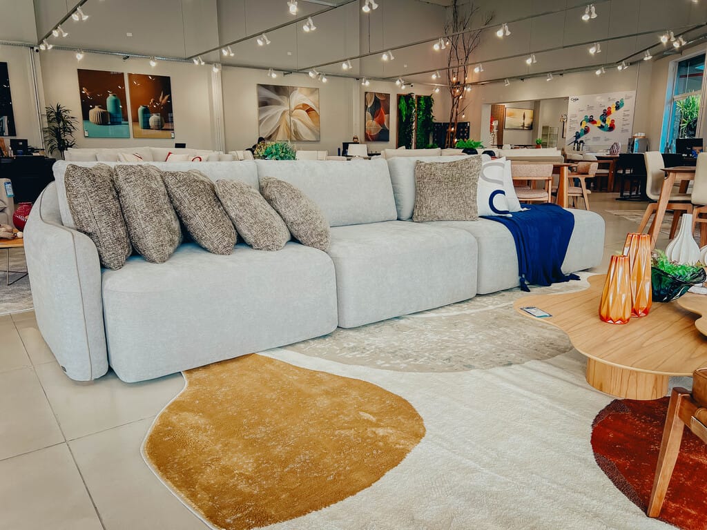 Sofá Schumacher Retrátil Modular Prata Viisão ampla e frontal do sofá modular Schumacher na cor prata com almofadas decorativas, posicionado em uma sala de estar elegante sobre um tapete claro.